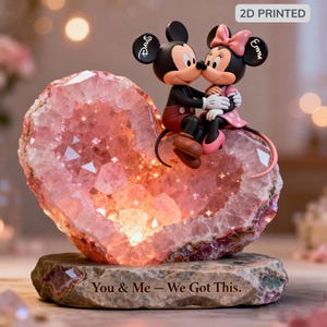 May include: A heart-shaped geode with Mickey and Minnie Mouse figurines. The pink geode sits on a stone base. The figurines are kissing. The base has the text "You & Me - We Got This".