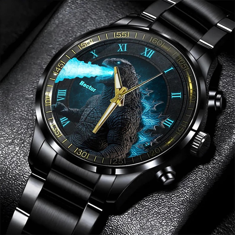 K&ouml;nnte beinhalten: Schwarze Armbanduhr mit Godzilla-Grafik auf dem Zifferblatt. Die Uhr hat goldfarbene Zeiger und ein schwarzes Metallarmband. Das Zifferblatt hat r&ouml;mische Ziffern und einen blauen Leuchteffekt.