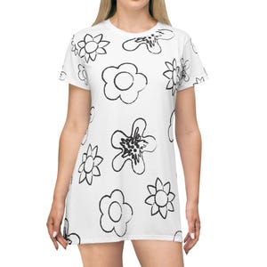 Könnte beinhalten: Weißes Kleid mit schwarzem Blumenmuster. Das Kleid hat einen Rundhalsausschnitt und kurze Ärmel. Das florale Design umfasst verschiedene Blumenformen in einem einfachen, umrissenen Stil. Das Kleid ist knielang.