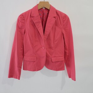 Op de afbeelding: Een roze blazer met een enkele knoopsluiting en twee zakken. De blazer heeft een licht gepofte mouw.