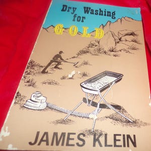 May include: A book titled "Dry Washing for GOLD" by James Klein. The cover features a cartoon illustration of a person panning for gold in a desert landscape. The book is about gold prospecting.