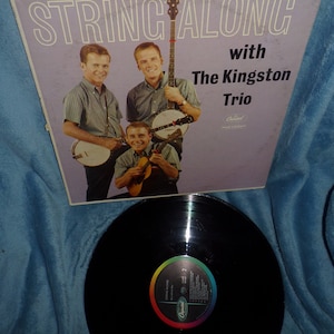 May include: A vintage vinyl record album cover featuring The Kingston Trio. The cover is purple and features a photo of the band members playing banjos. The album title is "String Along" with the band's name and "with The Kingston Trio" printed below.