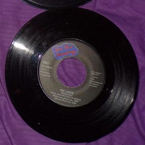 May include: Black vinyl record with a red and white label. The label says "Red Rose Speedway" and "My Love" by Paul McCartney & Wings. The record is 45 RPM and was recorded in England.