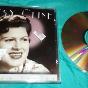May include: A CD case with a photo of Patsy Cline on the front. The case is silver and has the text "Platinum Series" on the bottom. The CD is visible through the clear plastic case.