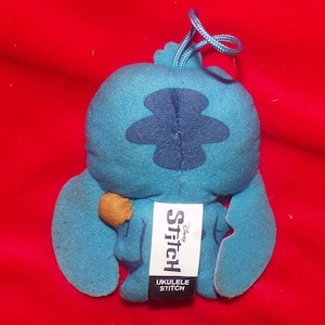 May include: Blue Stitch plush toy with a brown ukulele. The toy has a tag that says "Disney Stitch Ukulele Stitch".