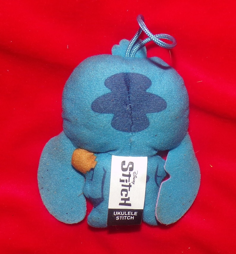 May include: Blue Stitch plush toy with a brown ukulele. The toy has a tag that says "Disney Stitch Ukulele Stitch".