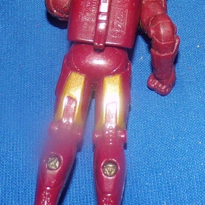 May include: Red and gold plastic action figure of Iron Man. The figure is posed with one arm raised and the other arm bent at the elbow. The figure has a detailed chest piece with the words "TM & &copy; 2007 Marvel" and "Made in China" printed on it. The figure also has a detailed back piece with the words "77501" and "Toy Biz" printed on it.