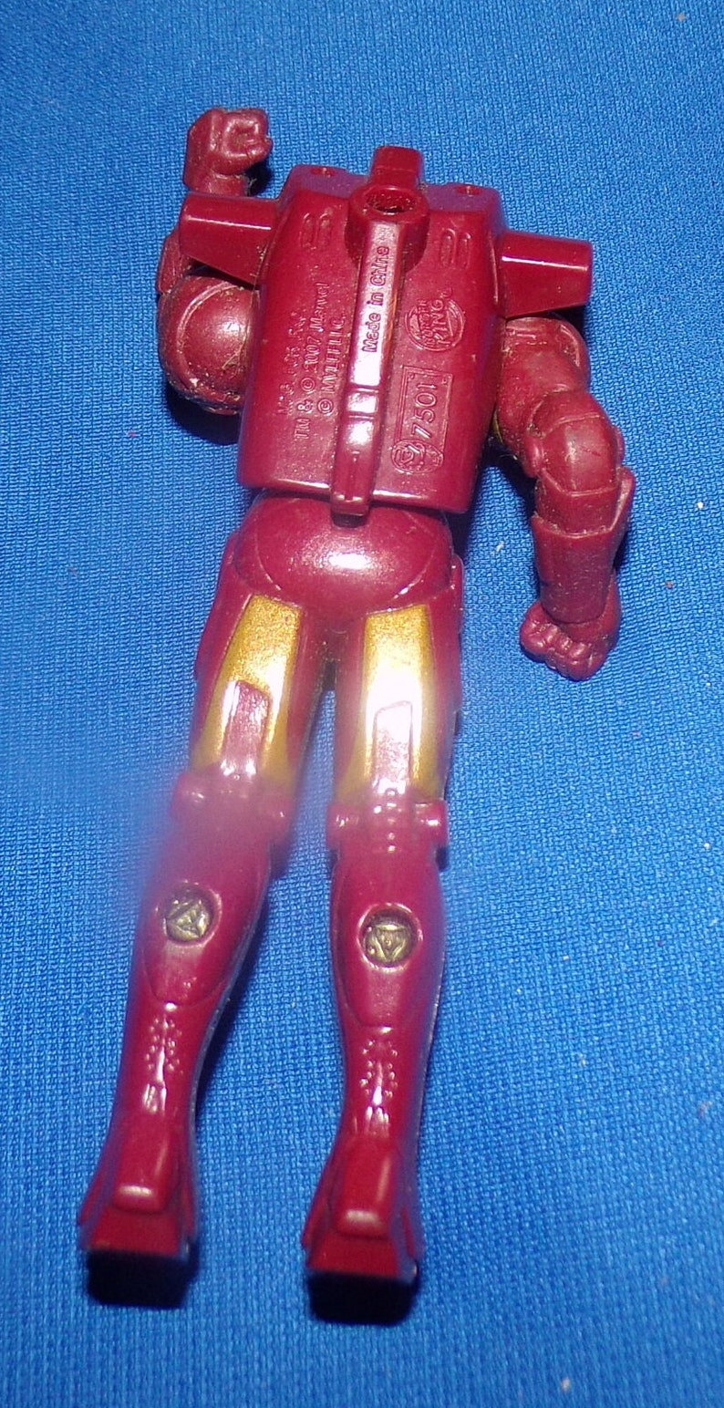 May include: Red and gold plastic action figure of Iron Man. The figure is posed with one arm raised and the other arm bent at the elbow. The figure has a detailed chest piece with the words "TM & &copy; 2007 Marvel" and "Made in China" printed on it. The figure also has a detailed back piece with the words "77501" and "Toy Biz" printed on it.