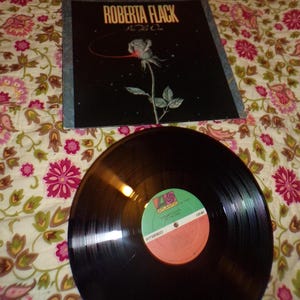 May include: A black vinyl record with a white label that says "Roberta Flack -  The First Time Ever I Saw Your Face" and "Atlantic" in a circle. The record is on a floral patterned fabric.