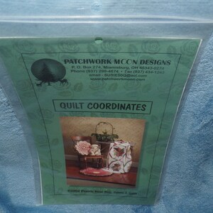May include: A green and white card with the text "Patchwork Moon Designs" and a picture of a quilt pattern called "Prairie Rose Hug". The card includes contact information for the company.