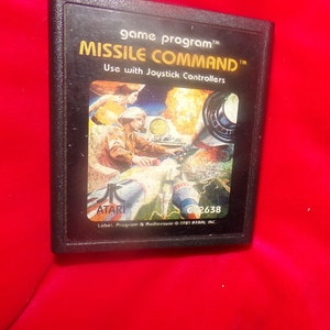May include: A black Atari game cartridge with a colorful image of a spaceship and a person in a spacesuit. The text on the cartridge reads "game program™ MISSILE COMMAND™ Use with Joystick Controllers ATARI® C2638 Label, Program & Audiovisual © 1981 ATARI, INC."