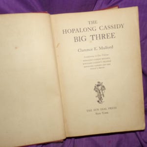 May include: A vintage book titled "The Hopalong Cassidy Big Three" by Clarence E. Mulford. The book cover features a black and white illustration of a cowboy riding a horse.