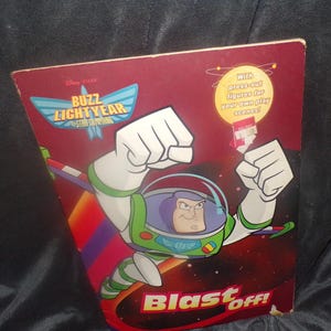 May include: A red and black Buzz Lightyear Star Command book cover. Buzz Lightyear is depicted in his space suit with his arms raised. The text "Blast Off!" is at the bottom. The cover also includes the text "With press-out figures for your own play scenes!"