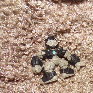 K&ouml;nnte beinhalten: Eine kleine Actionfigur eines roboterartigen Charakters. Die Figur ist haupts&auml;chlich schwarz, grau und beige, mit einem hellblauen kreisf&ouml;rmigen Design auf der Brust. Die Figur hat einen helm&auml;hnlichen Kopf und bewegliche Gliedma&szlig;en.