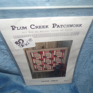 May include: A quilting pattern for a quilt called "Square Dance" from Plum Creek Patchwork. The pattern features a red and white geometric design.