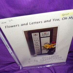 May include: A cross stitch pattern for a framed piece with the alphabet and flowers. The title of the pattern is "Flowers and Letters and You, Oh My!" and it is from Hillside Samplings.