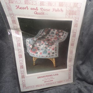 May include: A package for a "Heart and Nine Patch Quilt" pattern. The image shows a miniature chair draped with a quilt featuring heart and square patterns in red, green, and gray. The package has the text "Heart and Nine Patch Quilt" and "DESIGNERS LTD."