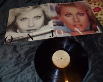 May include: A black vinyl record with a white label that says "Somebody's  Vow" and a picture of a woman on the cover. The cover is white with the text "Olivia Newton-John" and "On J.O.N." in black.