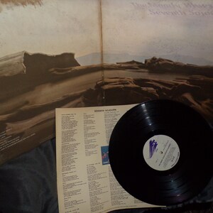 May include: A vinyl record album by The Moody Blues, titled "Seventh Sojourn." The album cover features a landscape painting in shades of brown and beige. The record is black with a white and purple label.