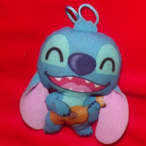 May include: Blue Stitch plush toy with purple ears, smiling and holding a brown guitar.