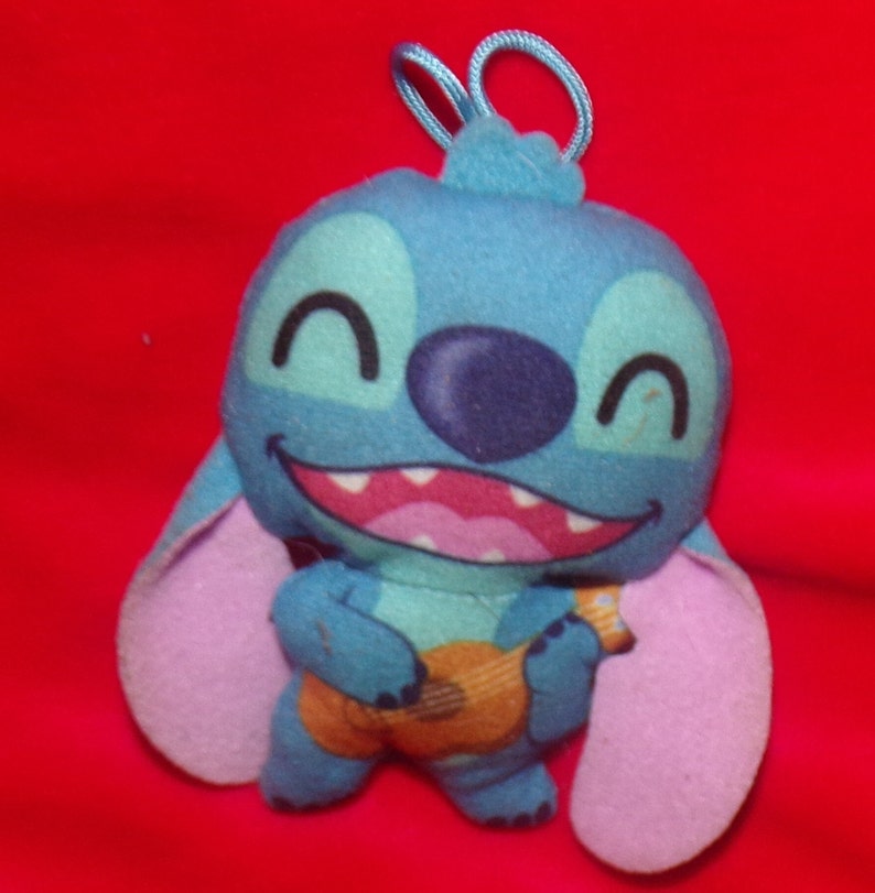 May include: Blue Stitch plush toy with purple ears, smiling and holding a brown guitar.