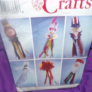 May include: A craft pattern featuring six different designs for making hanging decorations. The designs include a ghost, a bunny, a Santa Claus, a Uncle Sam, a star, and a jester. The pattern is printed on a white background with a blue border.