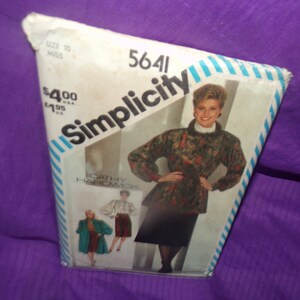 Può includere: Modello di cucito Simplicity numero 5641 per una giacca e una gonna. Il modello è per taglie da donna 10-18. Il modello mostra una donna che indossa una giacca con stampa floreale con una gonna nera e una camicetta bianca. Il modello mostra anche altre due donne che indossano diverse versioni della giacca e della gonna.