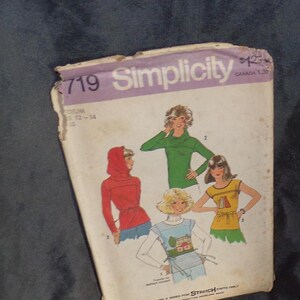 Op de afbeelding: Vintage Simplicity naaipatroon, maat medium, met illustraties van dames tops en een capuchonjas. De envelop is wit met paarse tekst en toont kledingontwerpen in rood, groen en geel.