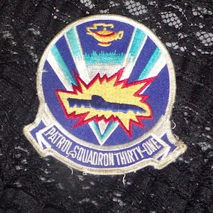 May include: A blue and white embroidered patch with a yellow and red explosion and a submarine. The text reads "Patrol Squadron Thirty-One".