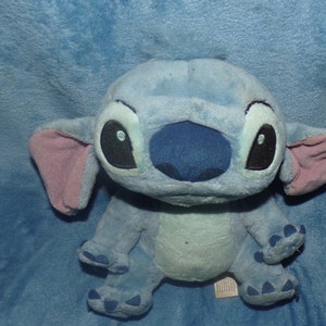 Puede incluir: Juguete de peluche azul y rosa de Stitch, personaje de la pel&iacute;cula de Disney Lilo & Stitch. El juguete tiene ojos grandes y negros y una nariz azul.