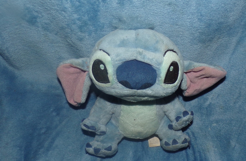 Puede incluir: Juguete de peluche azul y rosa de Stitch, personaje de la pel&iacute;cula de Disney Lilo & Stitch. El juguete tiene ojos grandes y negros y una nariz azul.
