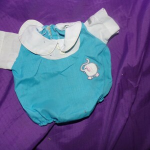 May include: A turquoise baby onesie with a white collar and short sleeves. An embroidered elephant with pink ears is on the front of the onesie.