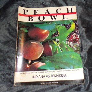 May include: A vintage Peach Bowl program cover featuring a photo of peaches and a football game. The text reads "PEACH BOWL", "TWENTIETH ANNUAL FOOTBALL CLASSIC JANUARY 2, 1988 ATLANTA, GEORGIA FIVE DOLLARS", "INDIANA VS. TENNESSEE", and "OFFICIAL SOUVENIR PROGRAM".