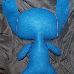 Puede incluir: Un peluche azul hecho a mano con orejas grandes, brazos peque&ntilde;os y piernas. El juguete est&aacute; hecho de tela suave y tiene costuras rosas claras alrededor de las orejas. El peluche es un personaje de una pel&iacute;cula de animaci&oacute;n popular.
