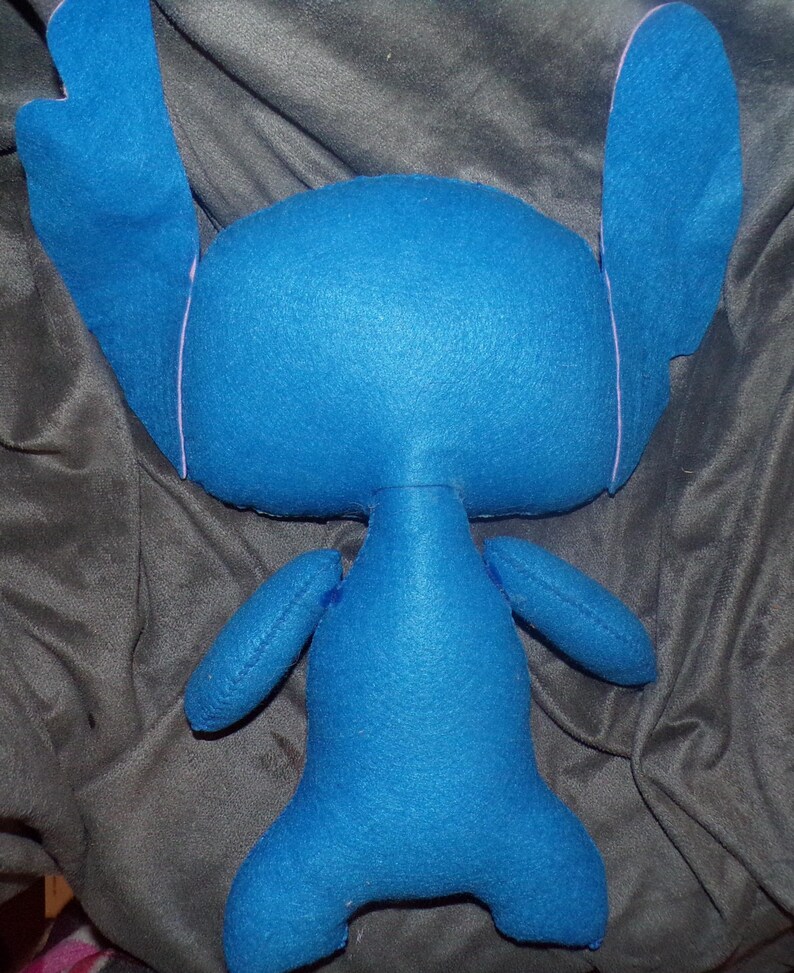 Puede incluir: Un peluche azul hecho a mano con orejas grandes, brazos peque&ntilde;os y piernas. El juguete est&aacute; hecho de tela suave y tiene costuras rosas claras alrededor de las orejas. El peluche es un personaje de una pel&iacute;cula de animaci&oacute;n popular.