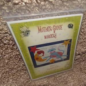 May include: A package featuring a "Mother Goose Nursery" design. The image includes a cartoon cow, moon, and stars with the text "Hey diddle diddle." The package has a green and yellow border.