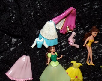 May include: A set of Disney Princess doll accessories, including a yellow dress, a pink skirt, a blue dress, a green dress, a pink cape, a white top, and two dolls.