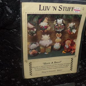 May include: A package of Luv 'N Stuff ball ornaments. The package features various fabric ornaments, including a mouse with a pumpkin, a bunny, and a turkey. The text on the package reads "HAVE A BALL!" and "They're Irresisti- BALL!"