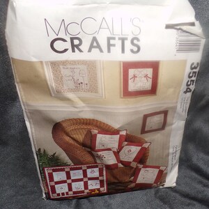 Op de afbeelding: Een McCall's Crafts patroonpakket met een thema voor huisdecoratie. Het pakket toont een rotan stoel met rood-witte geborduurde kussens en ingelijste kunstwerken. De omslag van het pakket toont de tekst "McCall's Crafts" en het nummer "3554".