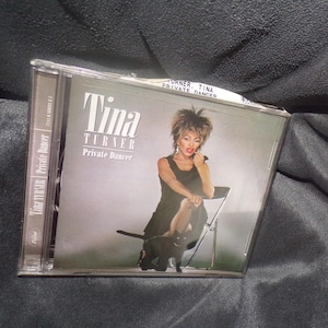 May include: A CD case featuring Tina Turner's album "Private Dancer." The album cover shows Tina Turner in a black dress, seated on a chair. The album title and artist's name are prominently displayed.