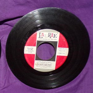 May include: Black vinyl record with a red label. The label has the text "Laurie Records Inc. New York" and "Little Bit O'Soul" by "The Music Explosion".