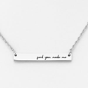 May include: A silver-colored necklace with a rectangular pendant. The pendant has the phrase "fuck you make me" engraved in a handwritten style. The necklace chain is a delicate, linked design.