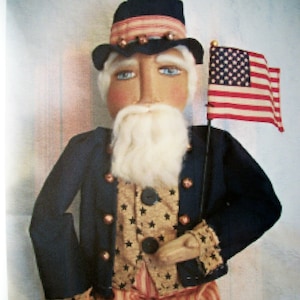 May include: A handmade patriotic doll dressed in a blue jacket, a vest with stars, and red and white striped pants. The doll is holding a small American flag.