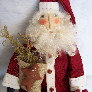 May include: A handmade rag doll Santa Claus wearing a red and white suit with a white beard and a gingerbread cookie in a burlap sack.