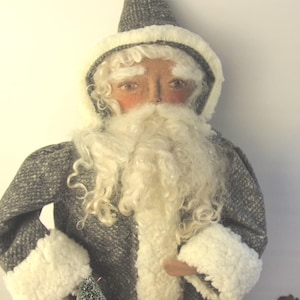 May include: A decorative Santa Claus figure with a gray coat and hat, trimmed with white faux fur. The figure has a long white beard and rosy cheeks, creating a festive holiday theme.