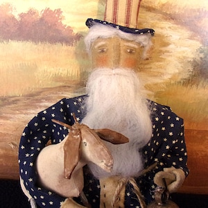 May include: A folk art doll of an elderly man with a long white beard, wearing a blue coat with white stars and a striped top hat. He holds a small goat and a bell.