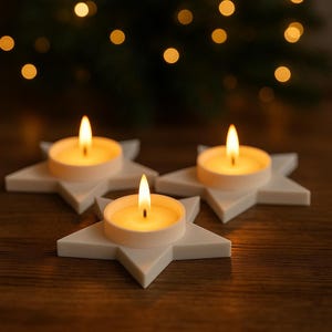 May include: Three lit tea light candles in white star-shaped holders. The candles have a warm, yellow glow, and the holders are arranged on a dark wooden surface. The background features blurred lights, creating a festive atmosphere.