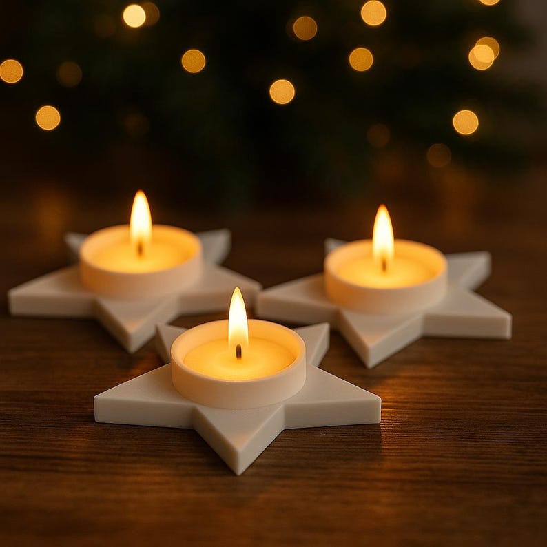 May include: Three lit tea light candles in white star-shaped holders. The candles have a warm, yellow glow, and the holders are arranged on a dark wooden surface. The background features blurred lights, creating a festive atmosphere.