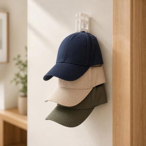 Può includere: Una pila di tre cappellini da baseball appesi a un gancio a parete bianco. Il cappellino superiore è blu navy, quello centrale è beige e quello inferiore è verde oliva. Ogni cappellino presenta una corona strutturata e una visiera curva.