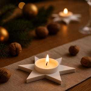 May include: A lit candle in a white star-shaped holder sits on a tan table runner. Walnuts and gold ornaments are scattered around the candle. The background is blurred with bokeh lights and greenery, creating a warm, festive atmosphere.